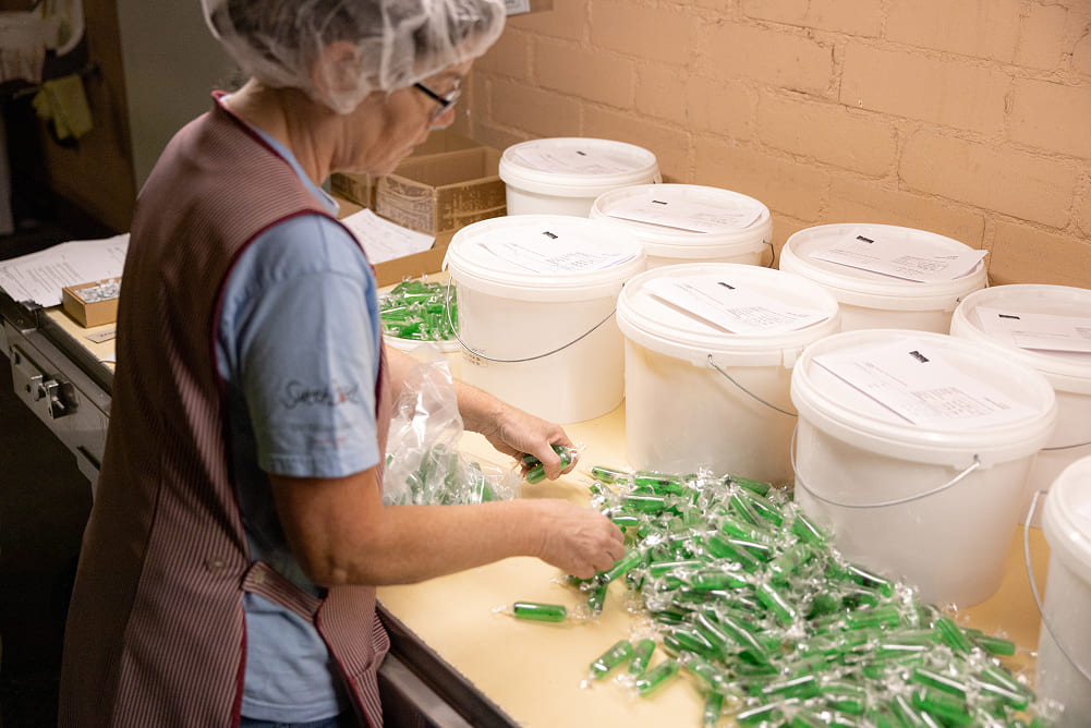 Mitarbeiterin bei Sweet Basel kontrolliert und etikettiert verpackte Süsswaren an einem Arbeitstisch.