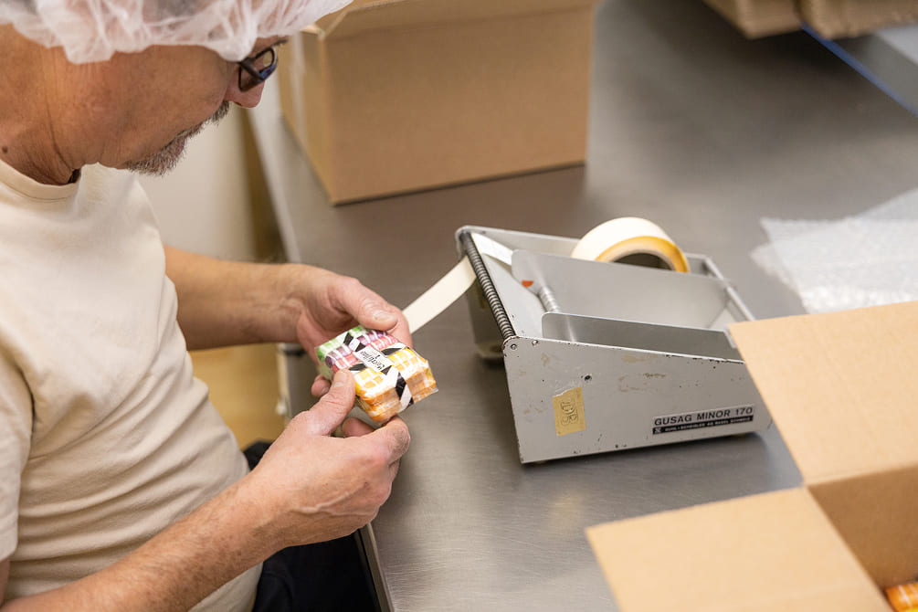 Mitarbeiter bei Sweet Basel kontrolliert und etikettiert verpackte Süsswaren an einem Arbeitstisch.