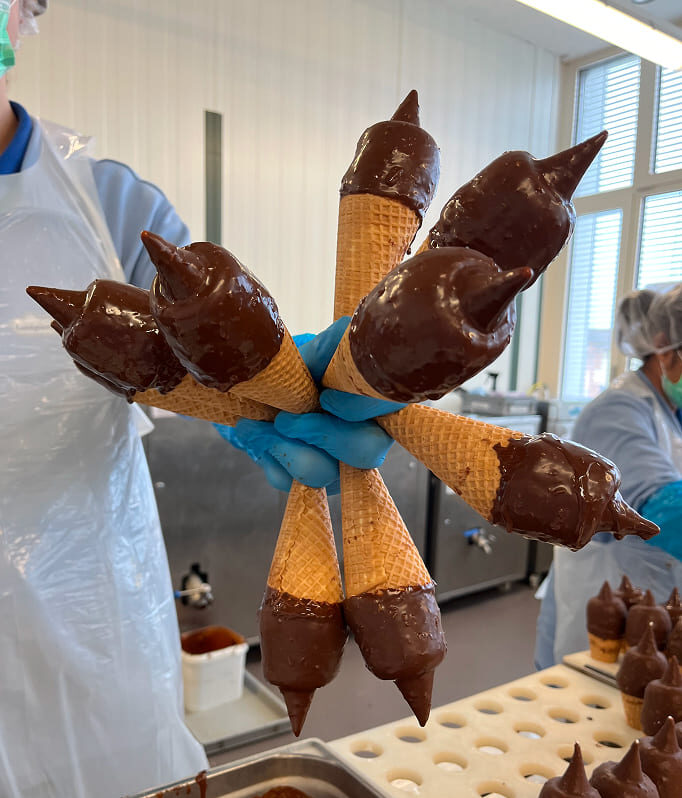 Mitarbeitende von Gelati Gasparini halten frisch mit Schokolade überzogene Waffelglacen in einer Produktionsküche.
