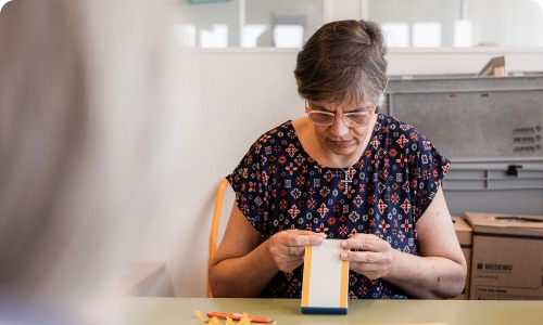 Mitarbeiterin konfektioniert und bearbeitet fokussiert Produkte von Hand an einem Arbeitstisch.